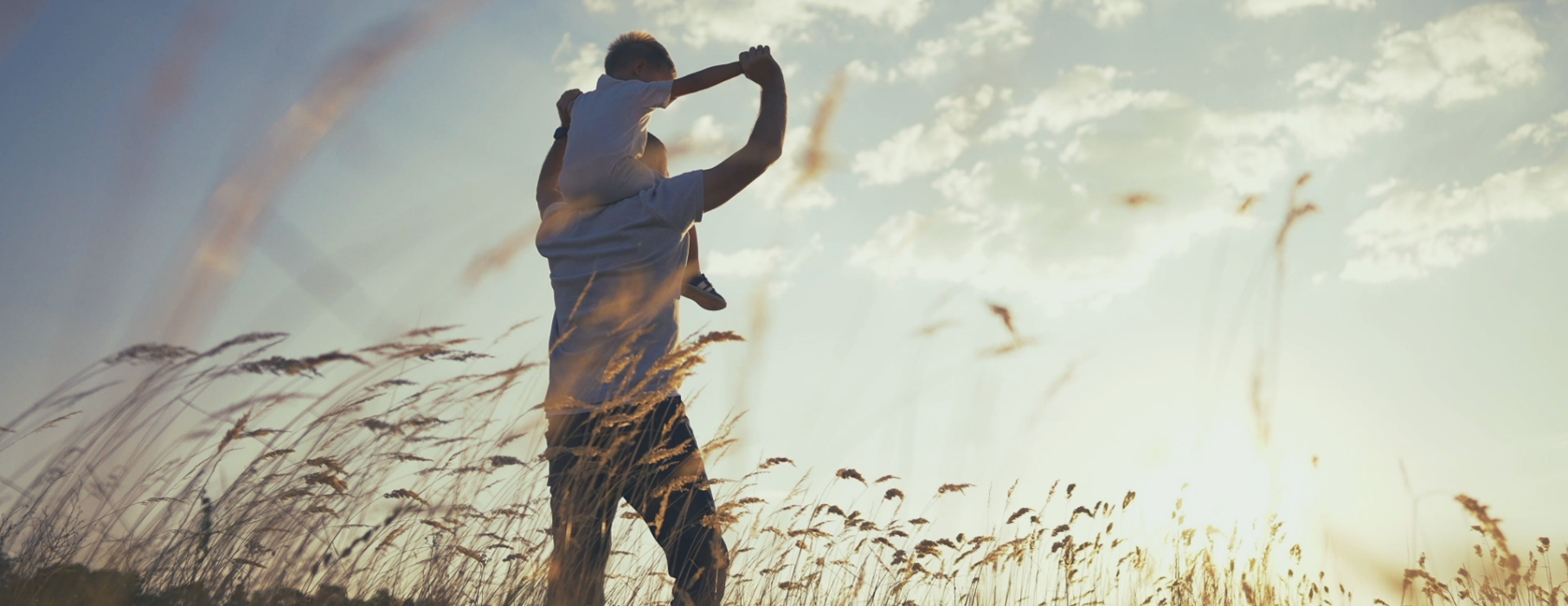 Son on fathers shoulders walking through field