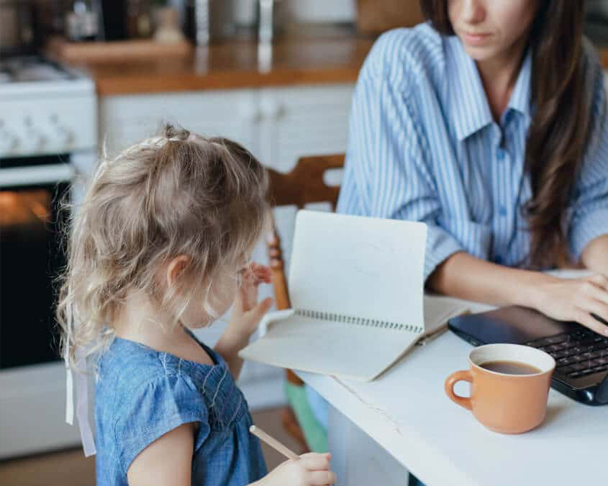 Mum on laptop with her daughter writing in a notebook